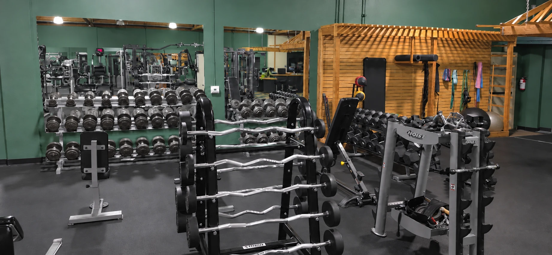 Dumbbells, barbells, and benches beside mirrored walls